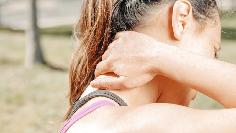Woman rubbing her neck in pain, representing TMJ and carpal tunnel symptoms